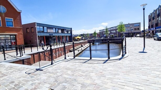 A cobblestone plaza with a canal, modern buildings, and a manhole cover. - Hotel Eckhardt (Uithuizen)