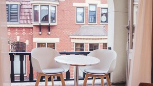 A balcony with a wooden table and two white chairs, overlooking a red brick building with multiple windows and a corner turret. - Hotel Eckhardt (Uithuizen)