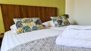 A hotel room with a bed, two pillows with a tropical leaf pattern, a grey quilted bedspread, and a white towel. - Hotel Eckhardt (Uithuizen)