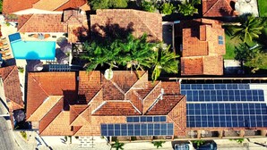 An aerial view of a residential area with a swimming pool, solar panels, and palm trees. - Pousada Solar de Geribá (Búzios)