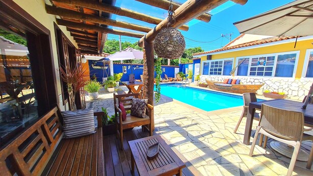 A wooden deck with a pool, outdoor furniture, and a stone wall. - Pousada Solar de Geribá (Búzios)