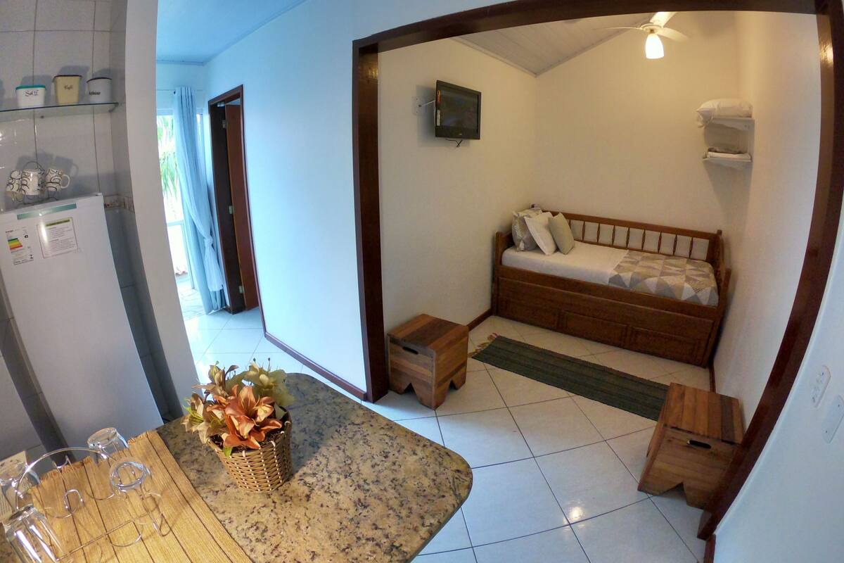 Une petite chambre comprenant un lit, une petite table, un réfrigérateur et un téléviseur.