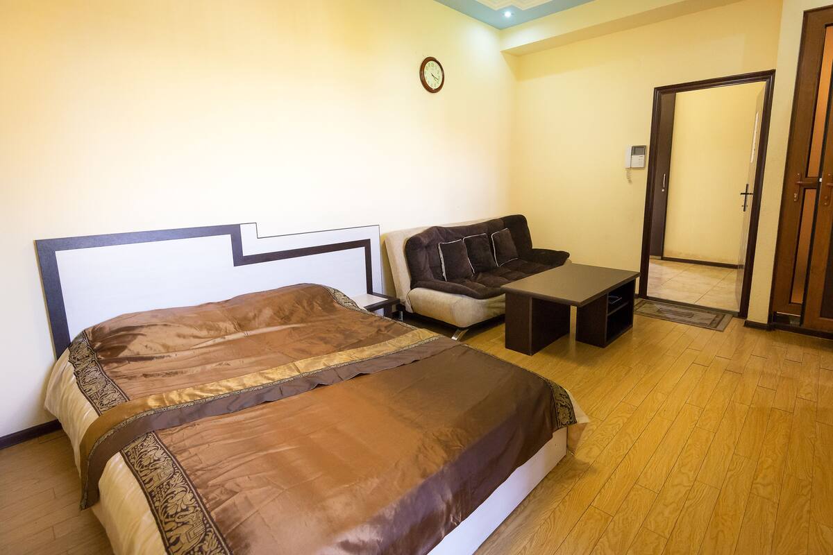A bedroom with a bed, a sofa, a small table, and a door.