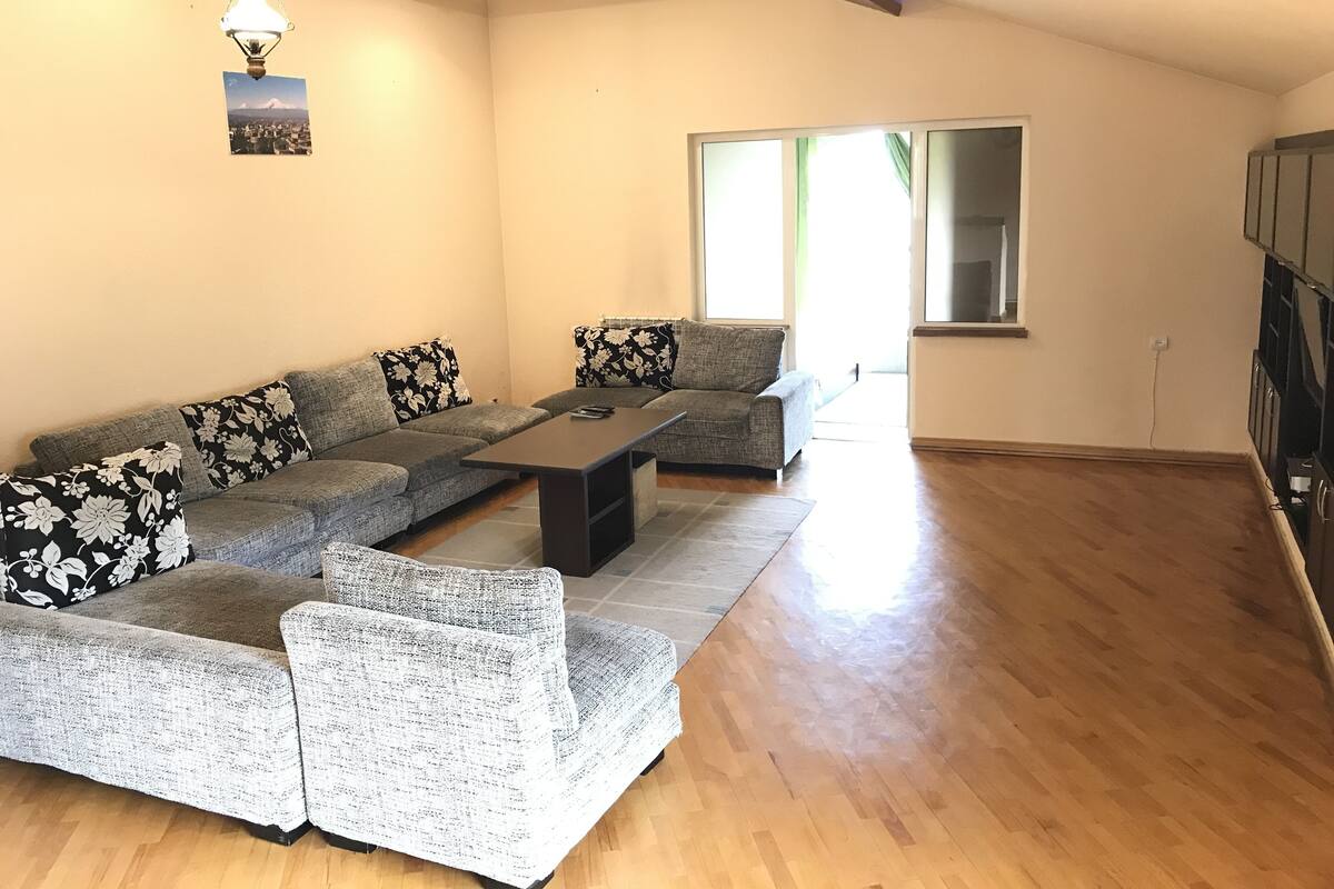 A modern living room with a grey sectional sofa, a coffee table, and a large window providing natural light.