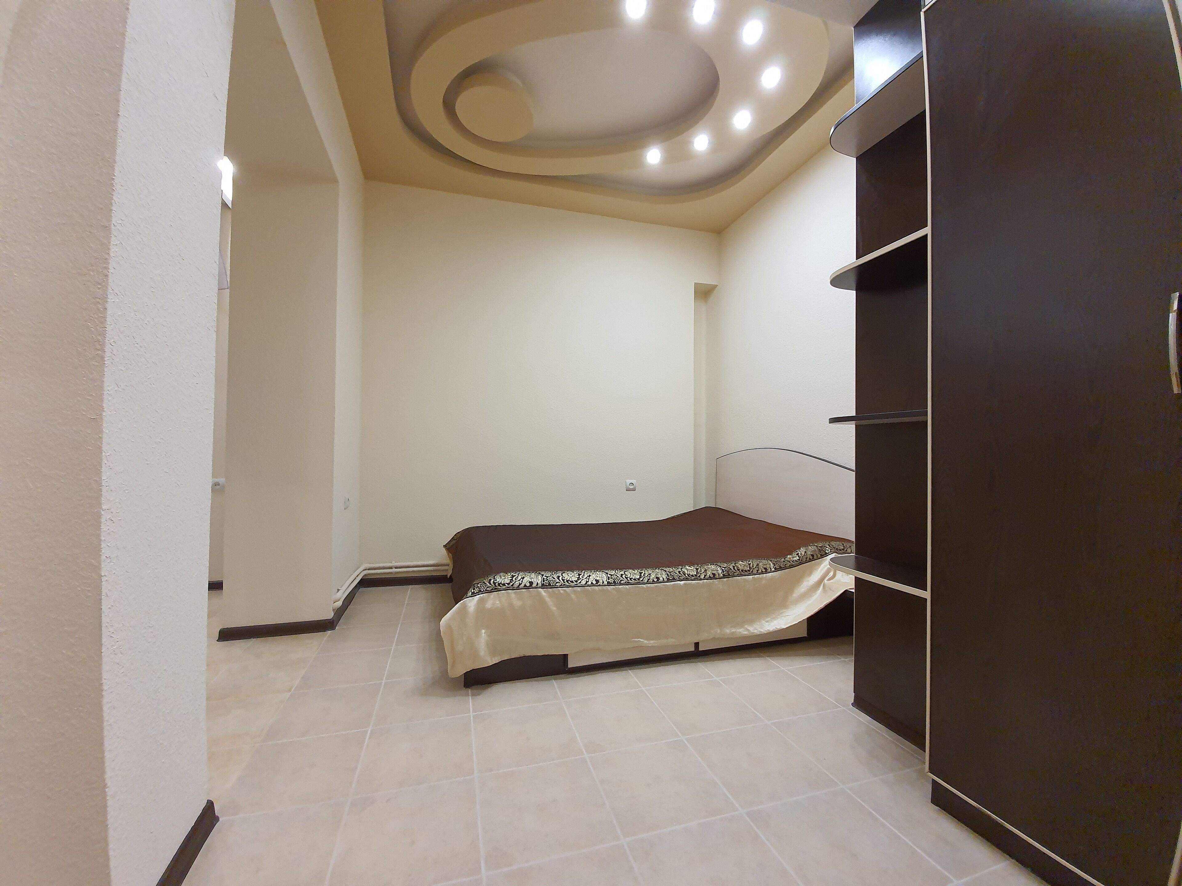 Ein Schlafzimmer mit Bett, Kleiderschrank und einer Decke mit runden Lampen.