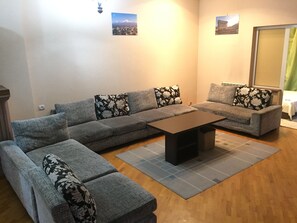 Un salon avec un canapé d’angle gris, une table basse et des coussins à motifs floraux.