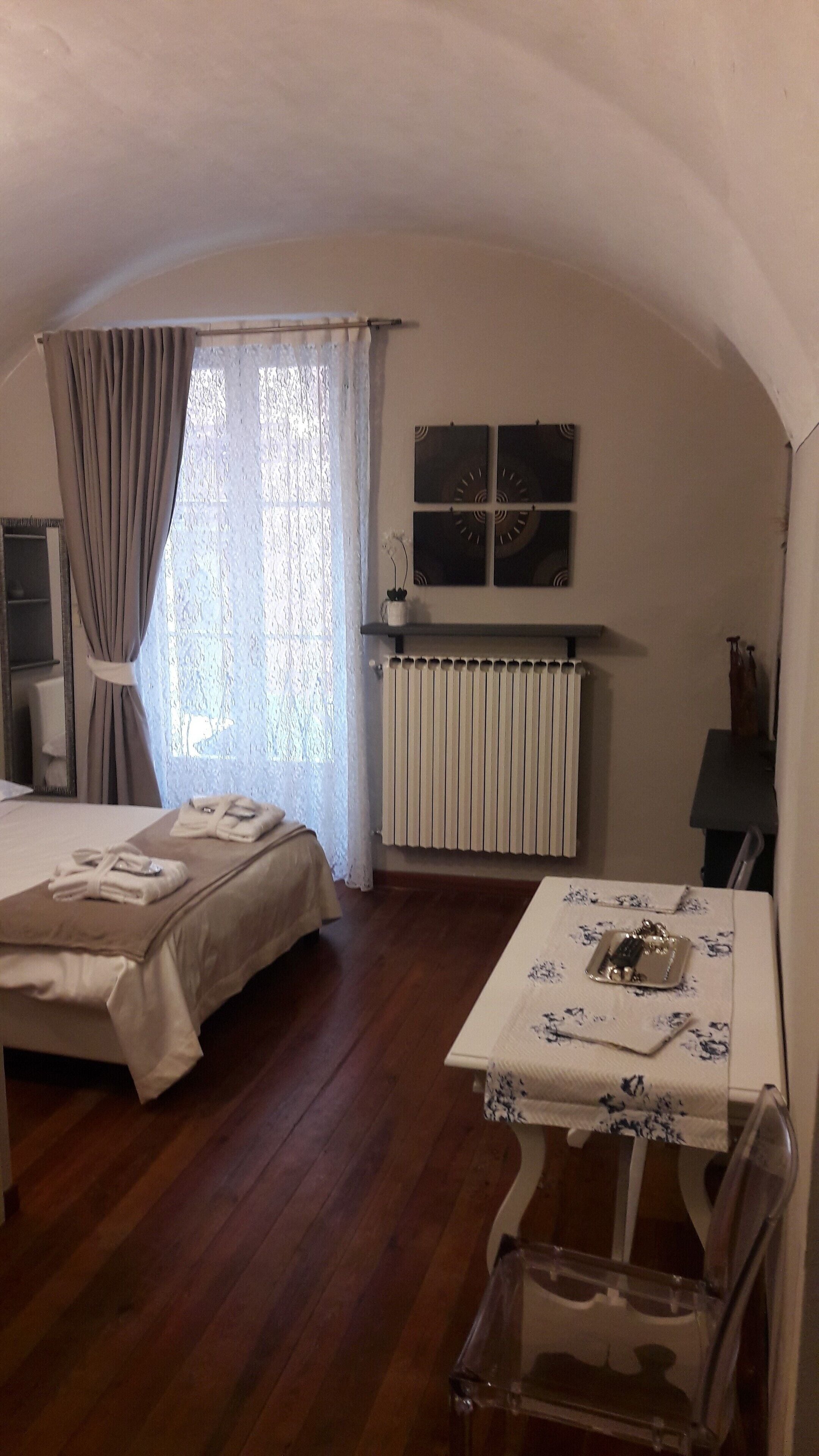 Ein Zimmer mit einem Bett, einem Tisch mit Blumenmuster-Tischdecke, einem Stuhl, einem Heizkörper und einem Fenster mit Vorhängen.
