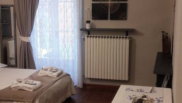 Ein Zimmer mit einem Bett, einem Tisch mit Blumenmuster-Tischdecke, einem Stuhl, einem Heizkörper und einem Fenster mit Vorhängen.