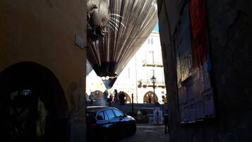 Un callejón estrecho con un globo aerostático al fondo, un coche aparcado y un edificio con carteles en la pared.