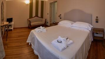 A hotel room with a large bed, a wooden floor, a chair, a desk with a television, and a mirror.