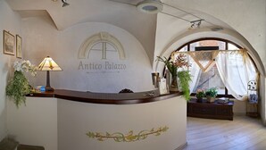 A reception desk with a lamp, framed pictures, and a sign reading "Antico Palazzo". - Antico Palazzo (Mondovi)