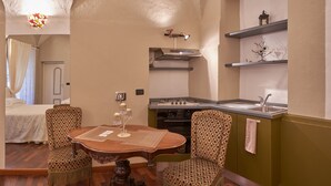 A cozy room with a dining table, two patterned chairs, a kitchen area with a stove and sink, and a bed with a canopy. - Antico Palazzo (Mondovi)