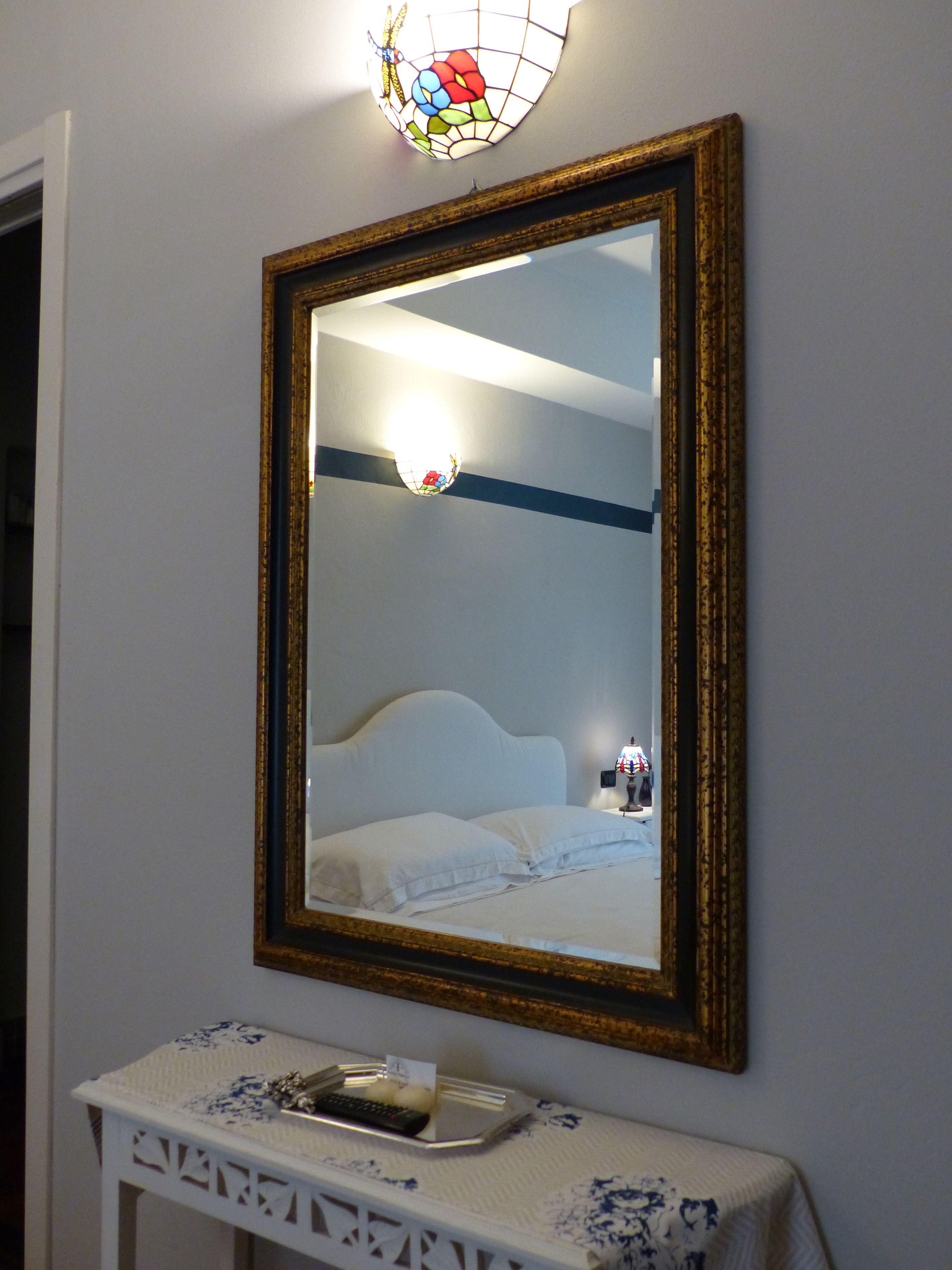 A room with a bed, a bedside table with a lamp, and a wall-mounted mirror.