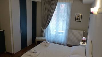 A hotel room with a bed, a nightstand, a lamp, a window with curtains, a radiator, and a door with a striped pattern.