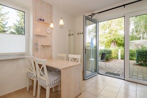 Un coin repas avec une table et des chaises en bois, une horloge, et une vue sur un jardin extérieur, visible à travers une porte vitrée.