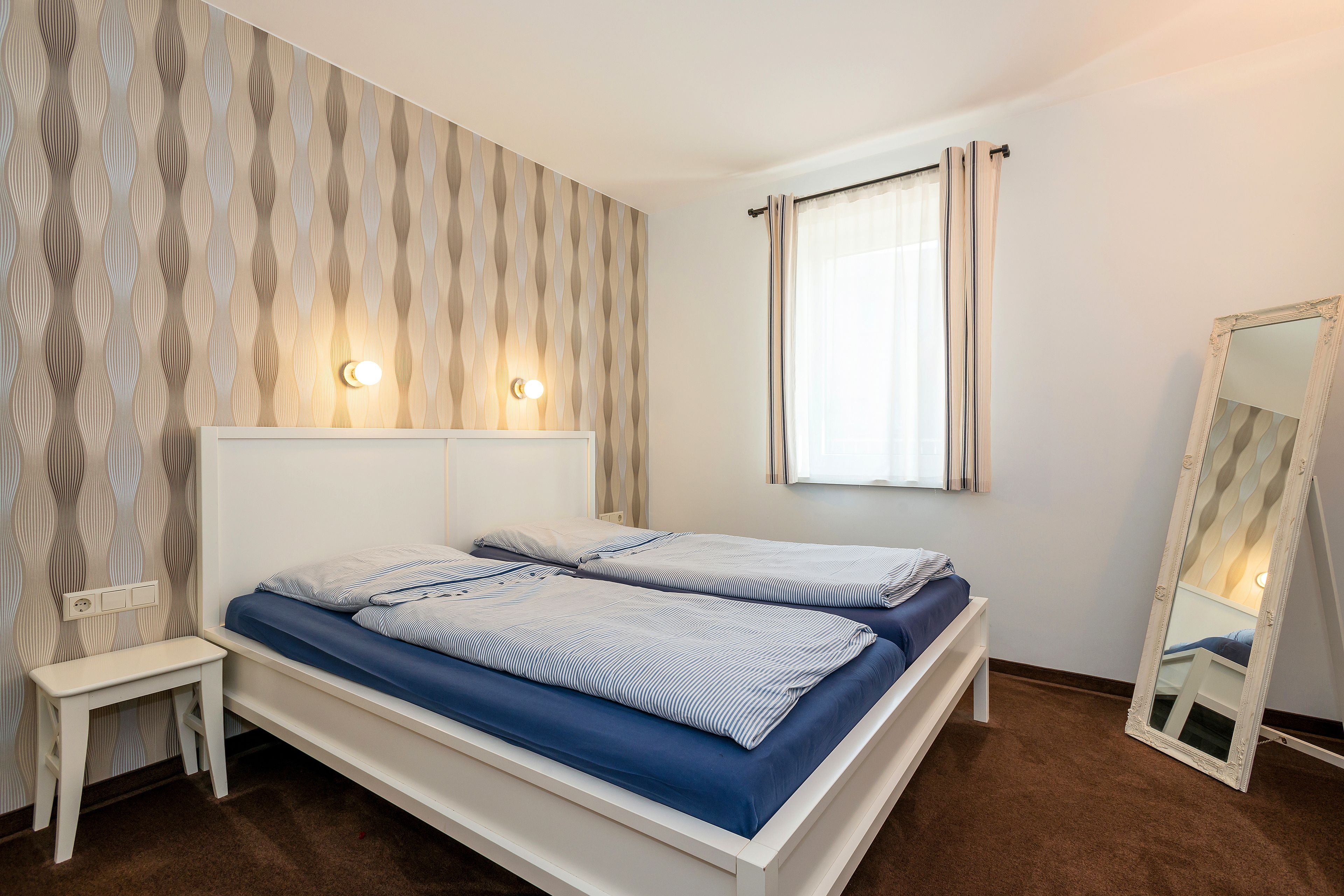 A bedroom with two single beds, a bedside table, a mirror, and a window with curtains.