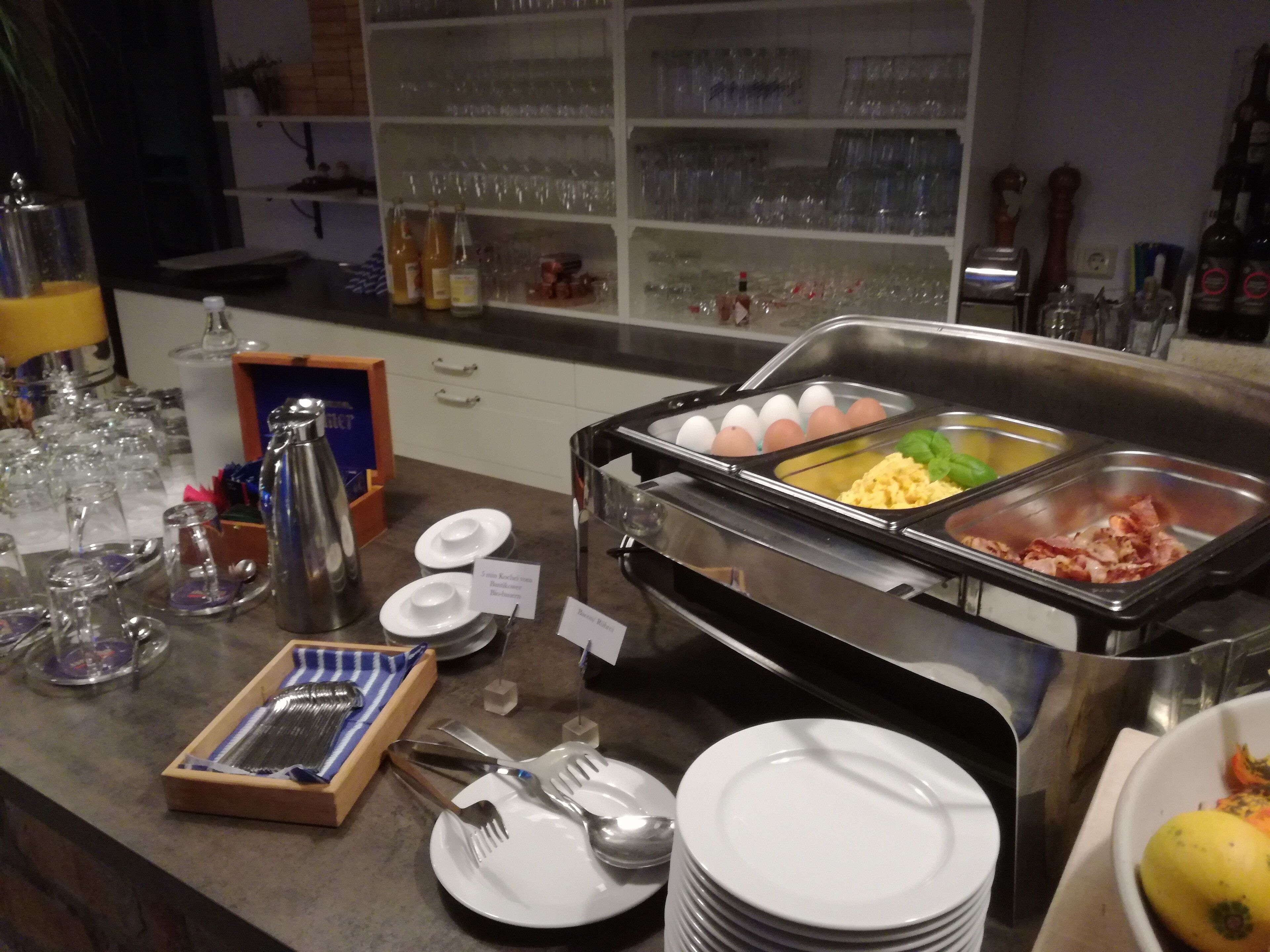 A buffet setup with various food items, including eggs, scrambled eggs, and bacon.