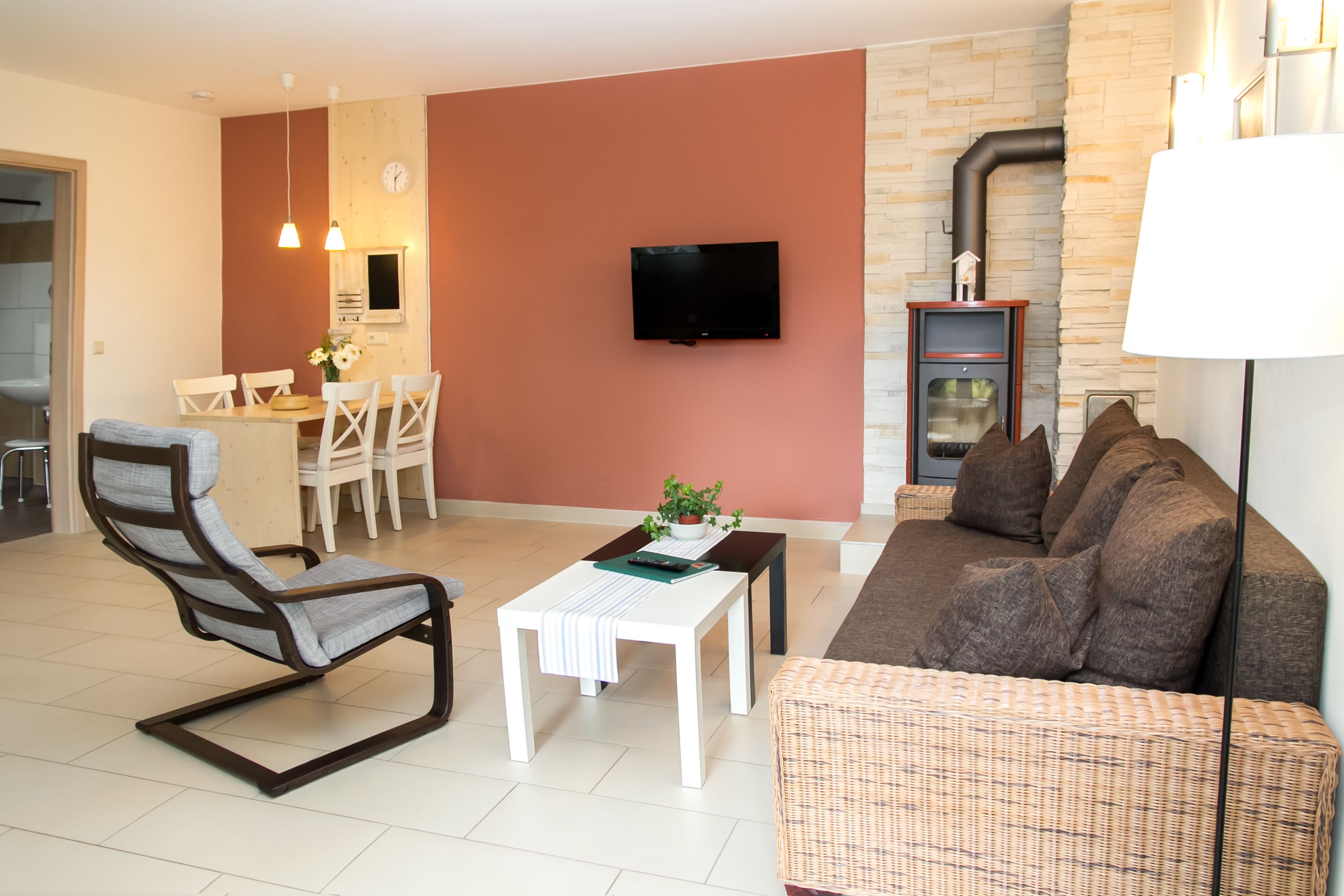 Una sala de estar moderna con un sofá, una silla, una mesa de comedor con sillas, un televisor montado en la pared y una chimenea.