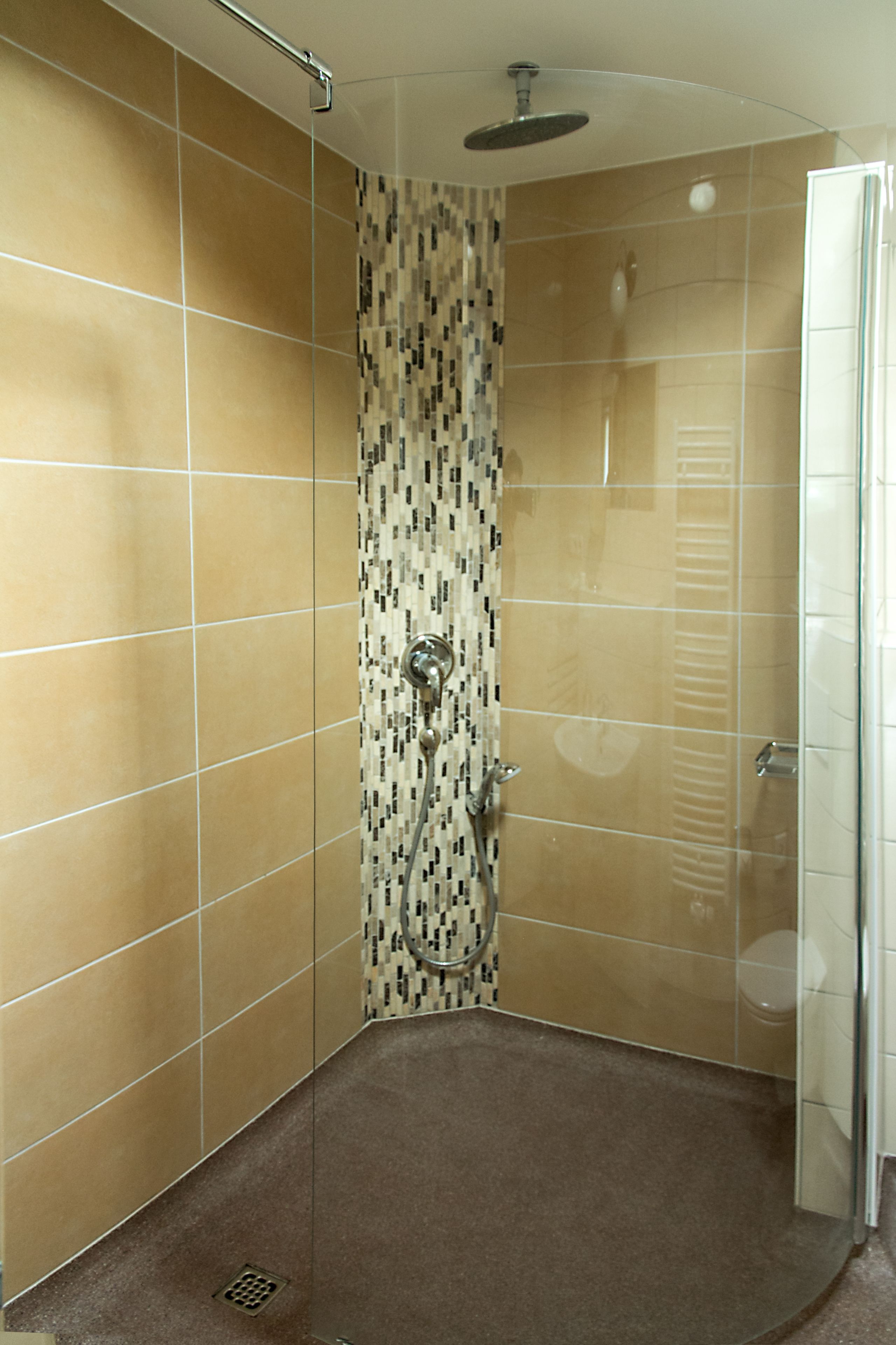 Um chuveiro no canto com paredes revestidas de azulejos, um chuveiro e uma porta de vidro.