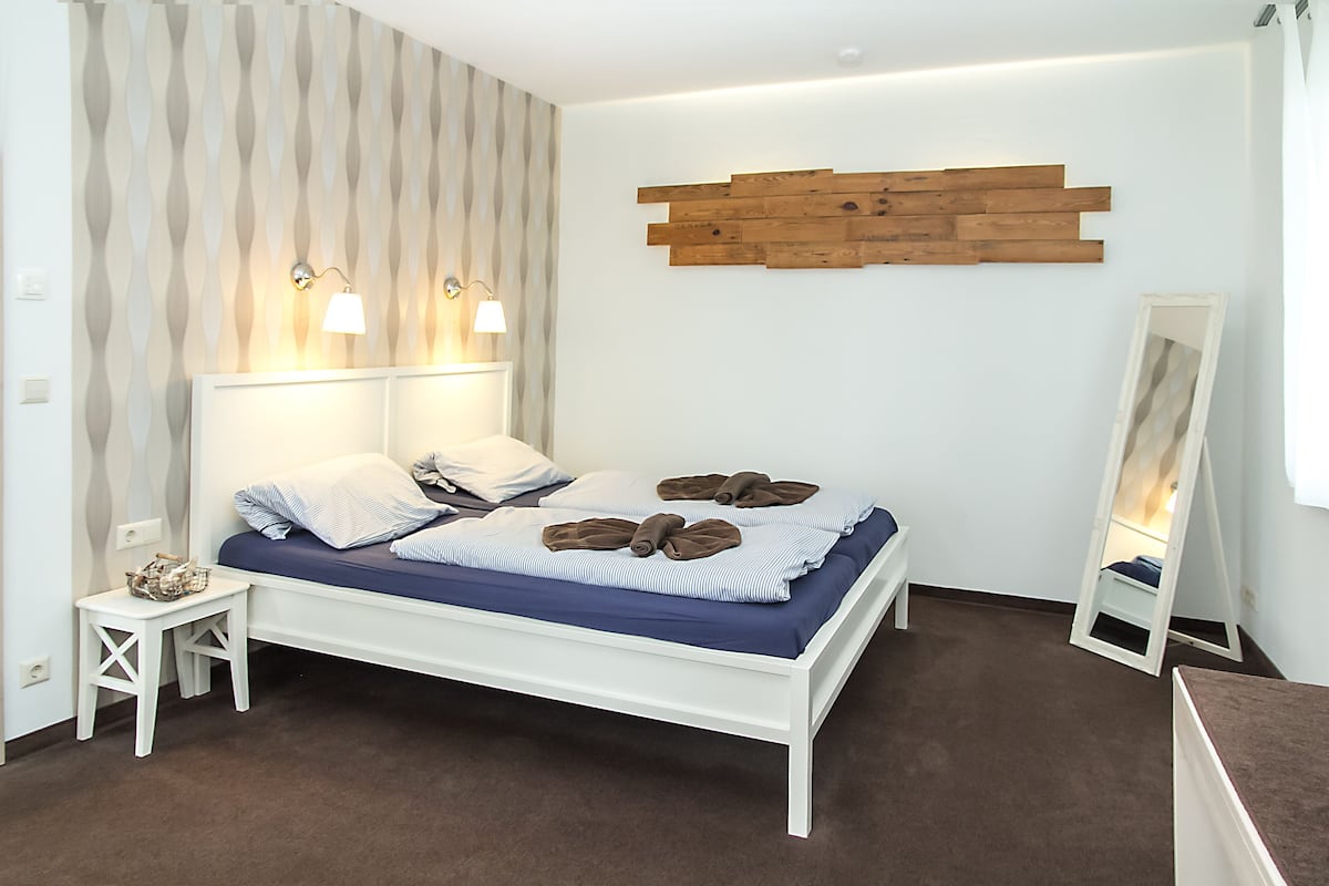 A neatly arranged bedroom with a bed, bedside tables, a wall-mounted light fixture, and a mirror.
