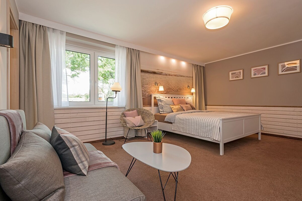 A bedroom with a bed, a sofa, a small table, and a floor lamp.