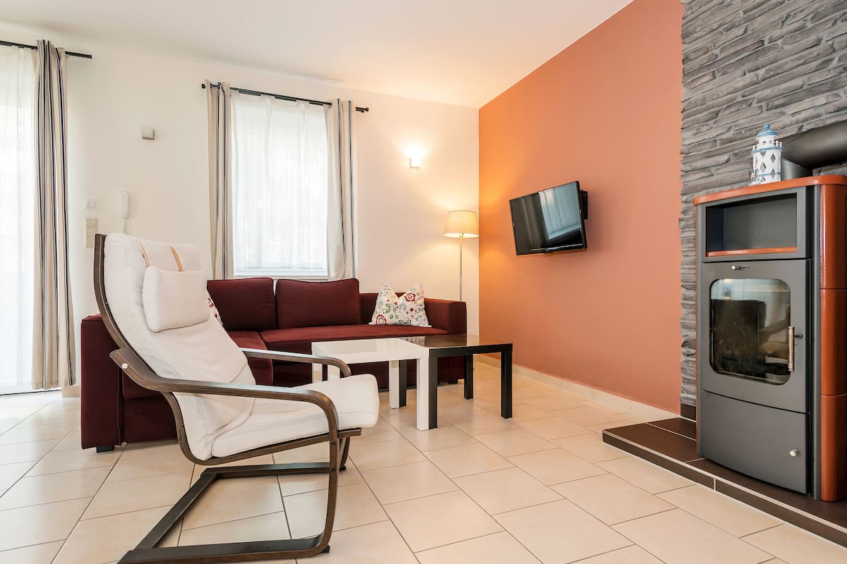 A modern living room with a sofa, a chair, a coffee table, a flat-screen TV mounted on the wall, and a built-in oven.