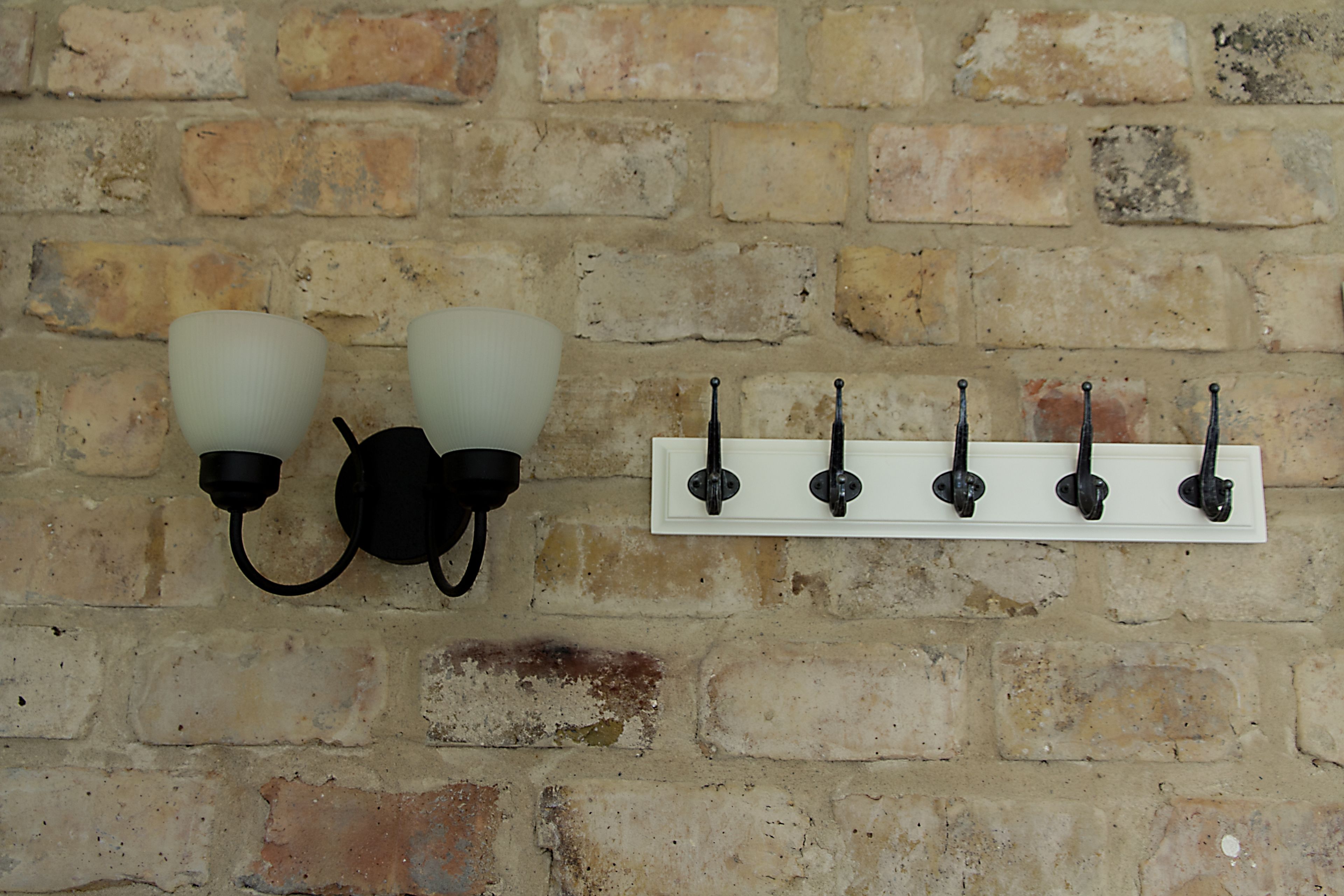 A wall-mounted light fixture with two frosted glass shades and a white metal bracket with four hooks.