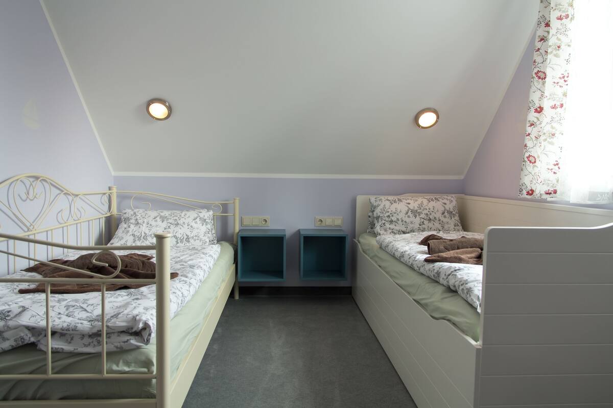 A bedroom with two single beds, a small desk, and a window with floral curtains.