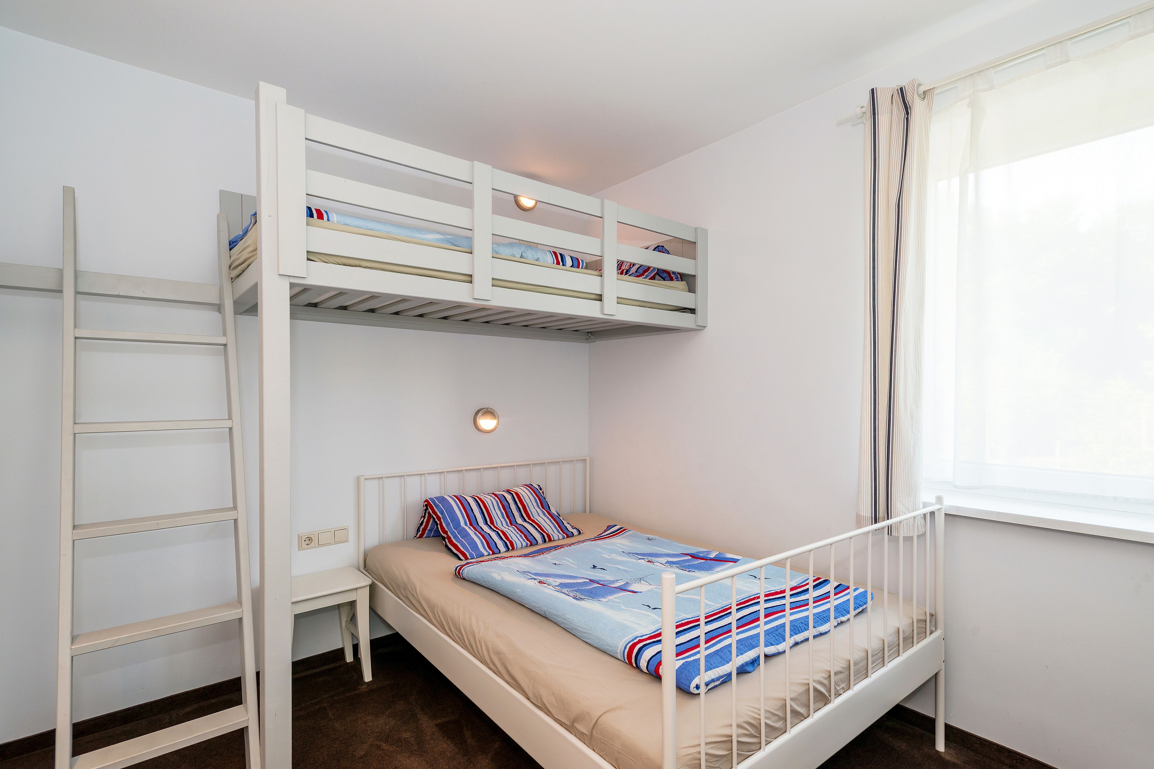 Una cama litera con escalera, una mesita de noche y una ventana con cortinas.