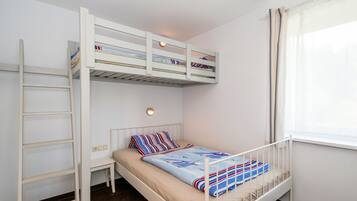 Una cama litera con escalera, una mesita de noche y una ventana con cortinas.
