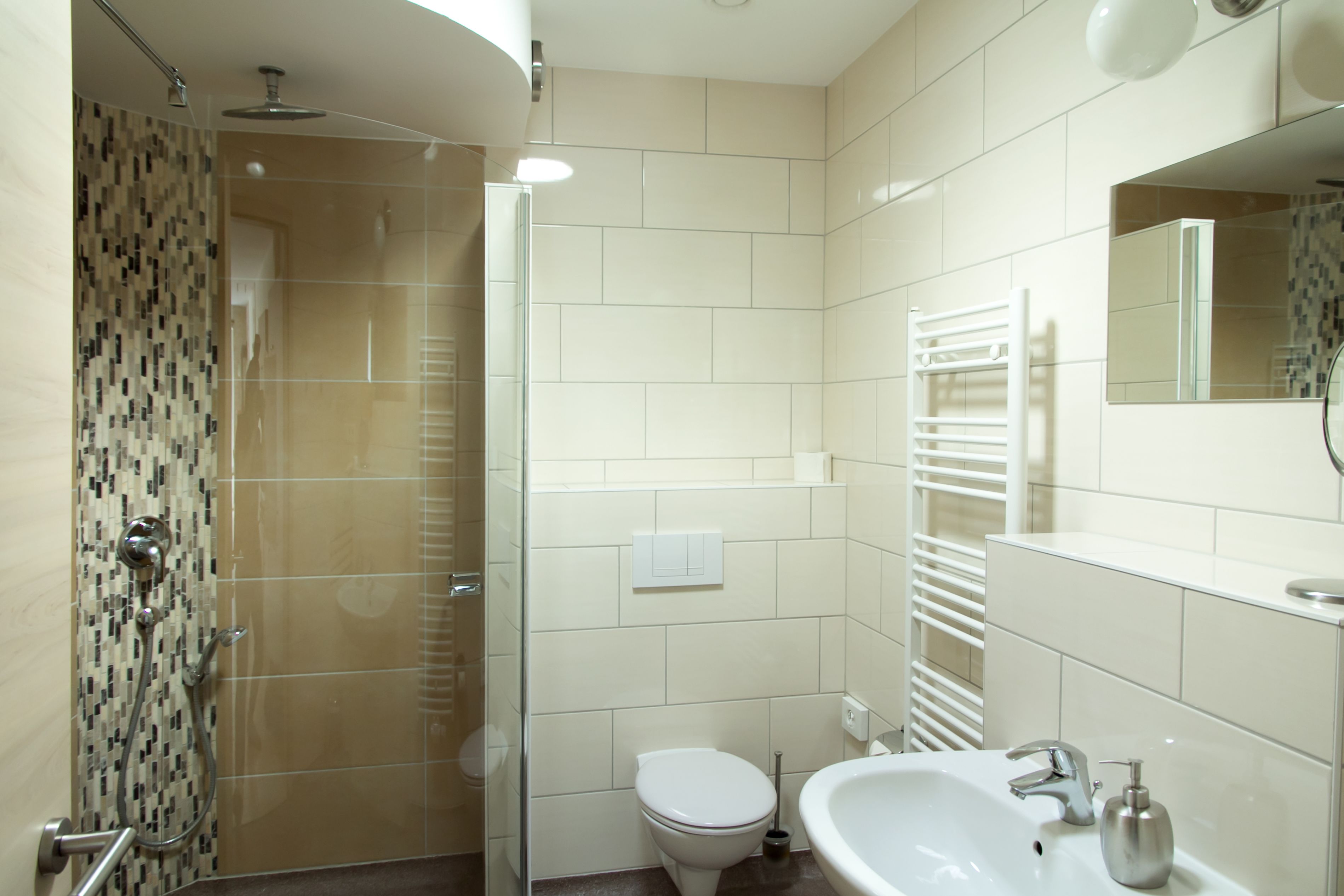 Un baño moderno con ducha de vidrio, inodoro, lavamanos con espejo y toallero.