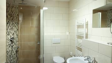 Un baño moderno con ducha de vidrio, inodoro, lavamanos con espejo y toallero.