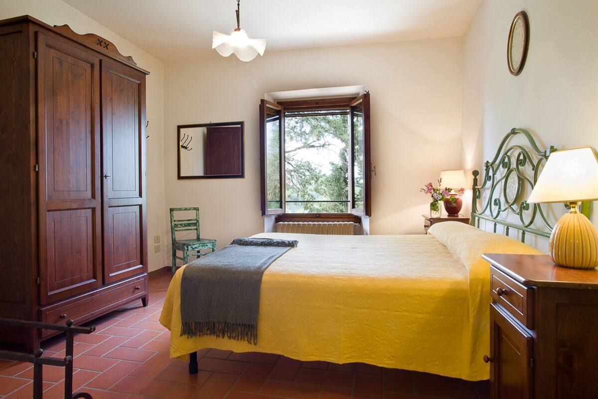 A bedroom with a bed, a wardrobe, a window with a view, a bedside table with a lamp, and a radiator.