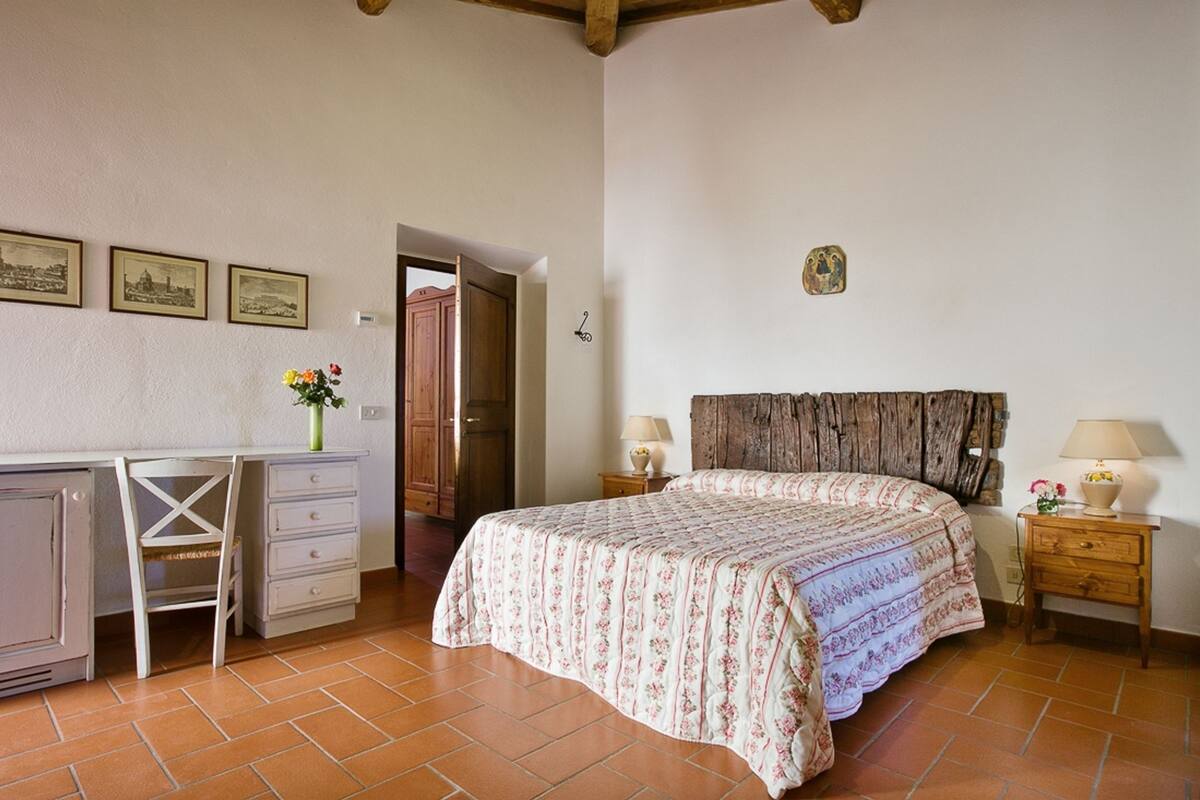 A bedroom with a bed, a desk, and a chair. There are two bedside tables with lamps.