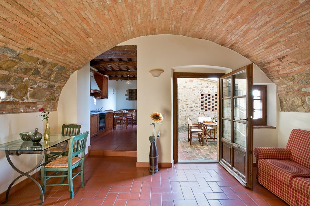 A rustic interior with a stone archway leading to a dining area and a kitchen.