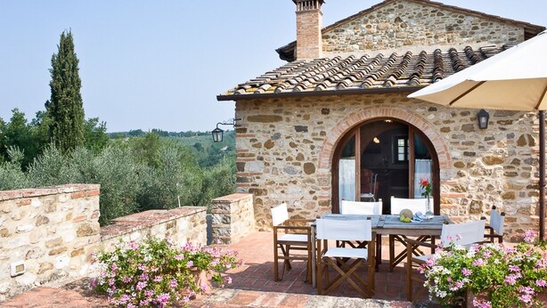 A stone building with a tiled roof, an arched doorway, and a table with chairs outside. - I Greppi di Silli (San Casciano in Val di Pesa)