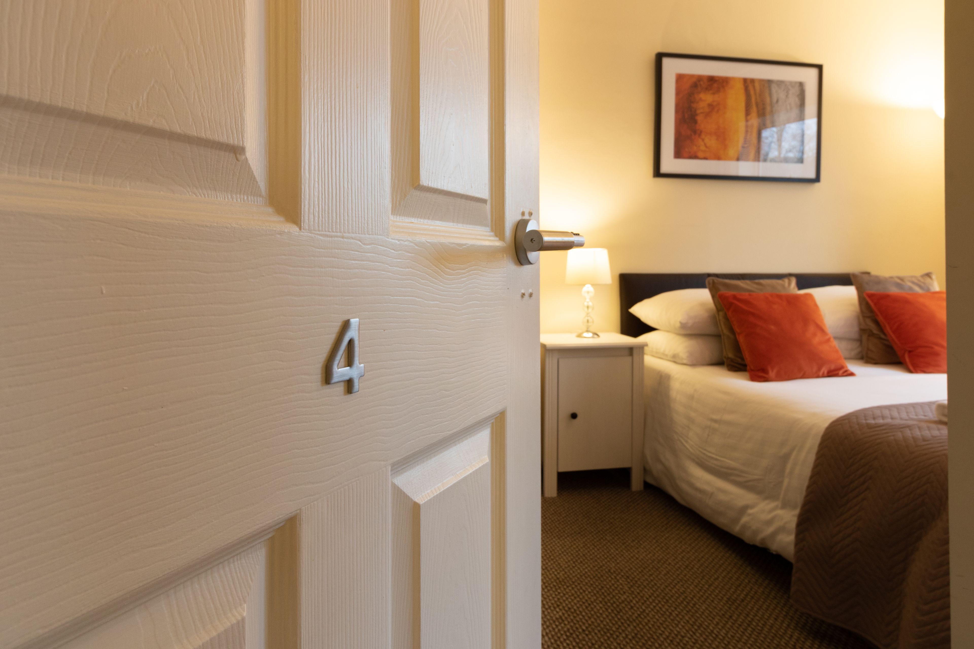A hotel room with a bed, a nightstand, a lamp, and a framed picture on the wall.