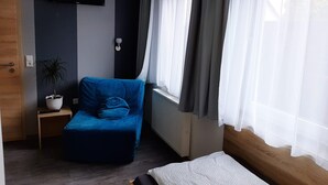 Une petite pièce moderne avec un canapé bleu, une petite table sur laquelle est posée une plante en pot, un lit avec un matelas blanc et un téléviseur fixé au mur.