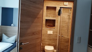 Une petite salle de bain avec une porte en bois, des toilettes et une petite étagère.
