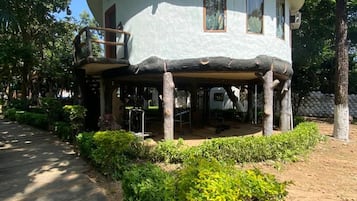 A two-story house with a covered porch, surrounded by greenery and trees.
