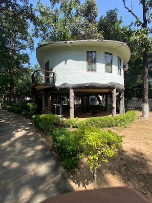 A two-story house with a covered porch, surrounded by greenery and trees. - Tigerwoods Kanha Resorts & Spa (Mandla)