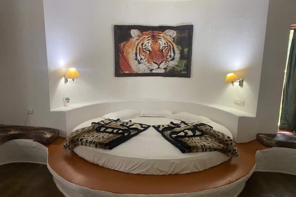 A circular bed with a tiger mural above, two wall-mounted lamps, and a small table with a lamp beside the bed.