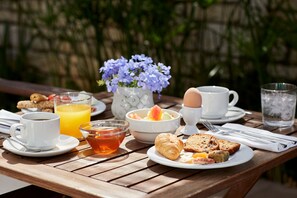 Une table de petit-déjeuner avec une tasse de café, un verre de jus d’orange, un bol de fruits, un croissant et une assiette de viennoiseries.