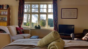 A cozy living room with a large window, a sofa, a television, and a bookshelf. - Beech Hill B&B (Northwich)