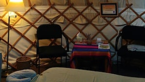A cozy interior of a yurt with a bed, two chairs, a small table with a colorful cloth, and a lamp. - Beech Hill B&B (Northwich)