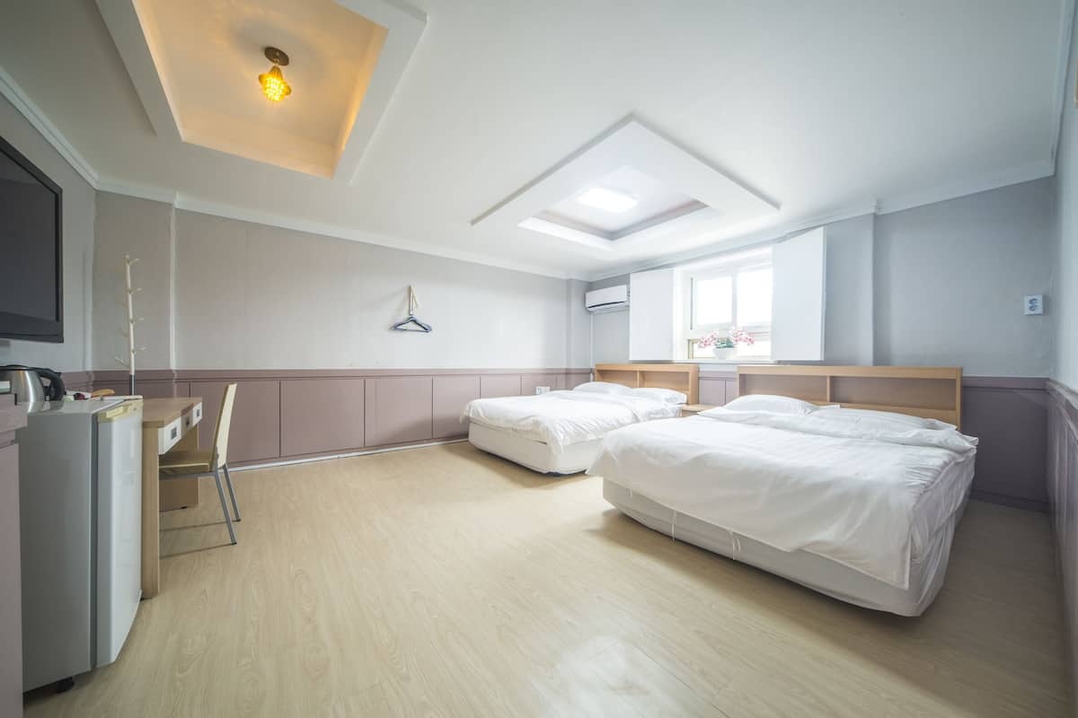 A hotel room with two beds, a desk, a chair, a TV, and a window with a view.