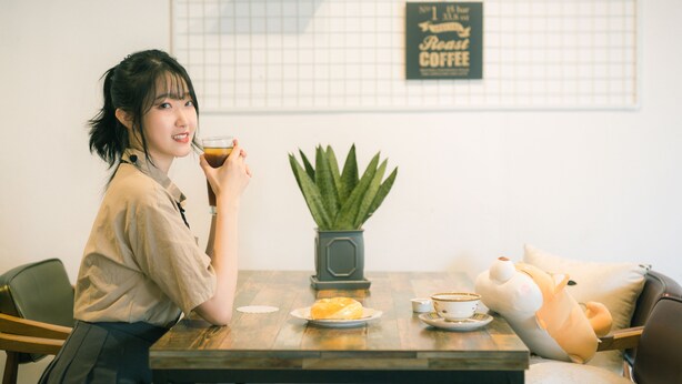 A person sitting at a table with a cup of coffee, a plate of food, and a potted plant.