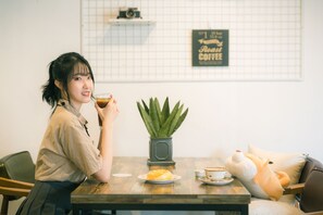 A person sitting at a table with a cup of coffee, a plate of food, and a potted plant. - Gyeong`s Business Hostel (Daegu)