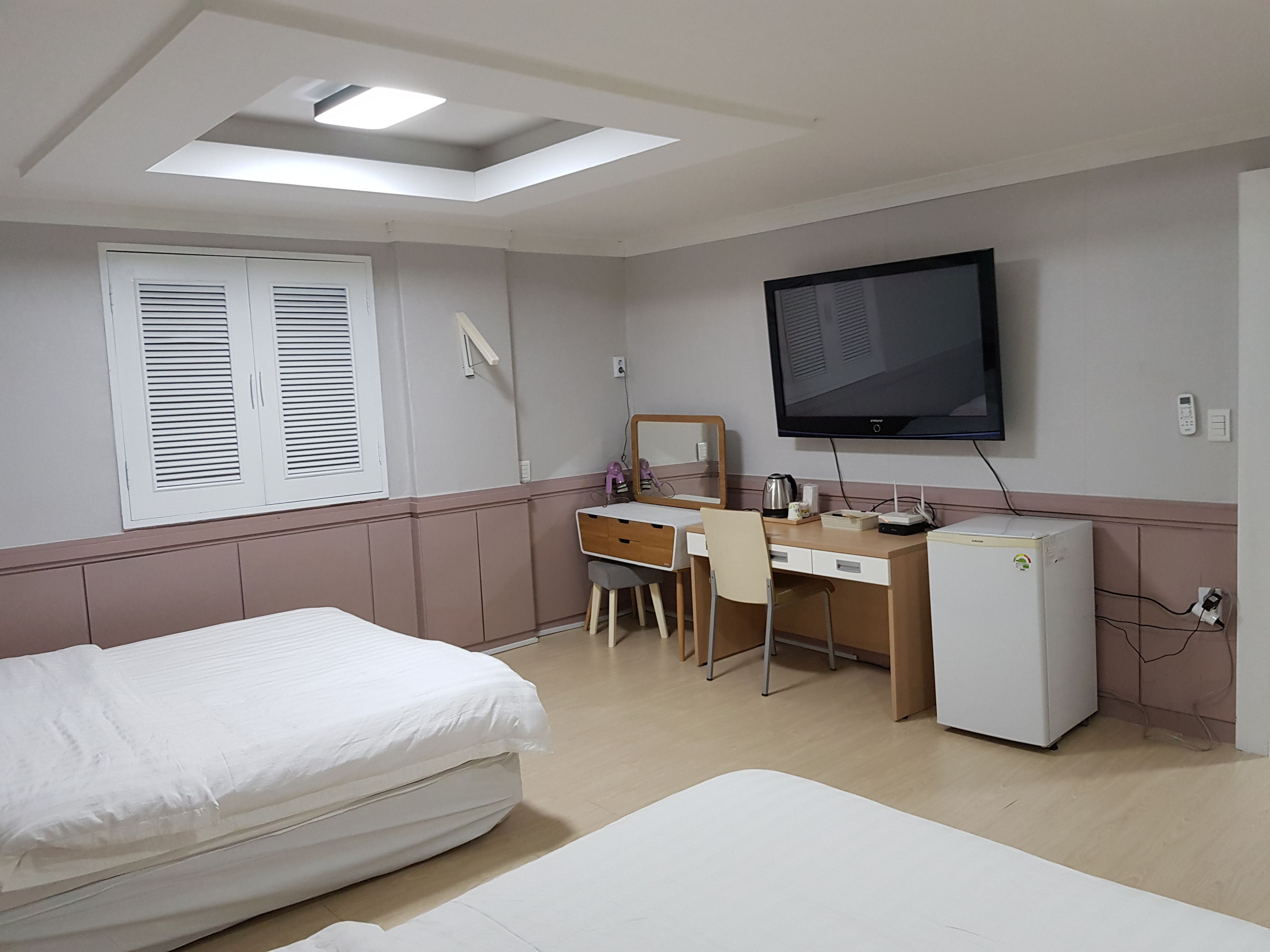 A hotel room with a bed, a desk with a chair, a television, and a refrigerator.