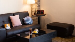 A modern living room with a black leather sofa, a small round table with a lamp, a radio, and a cactus.